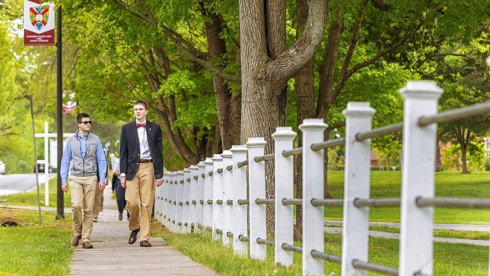 Two students walking along the H-SC fencerow that lines college road