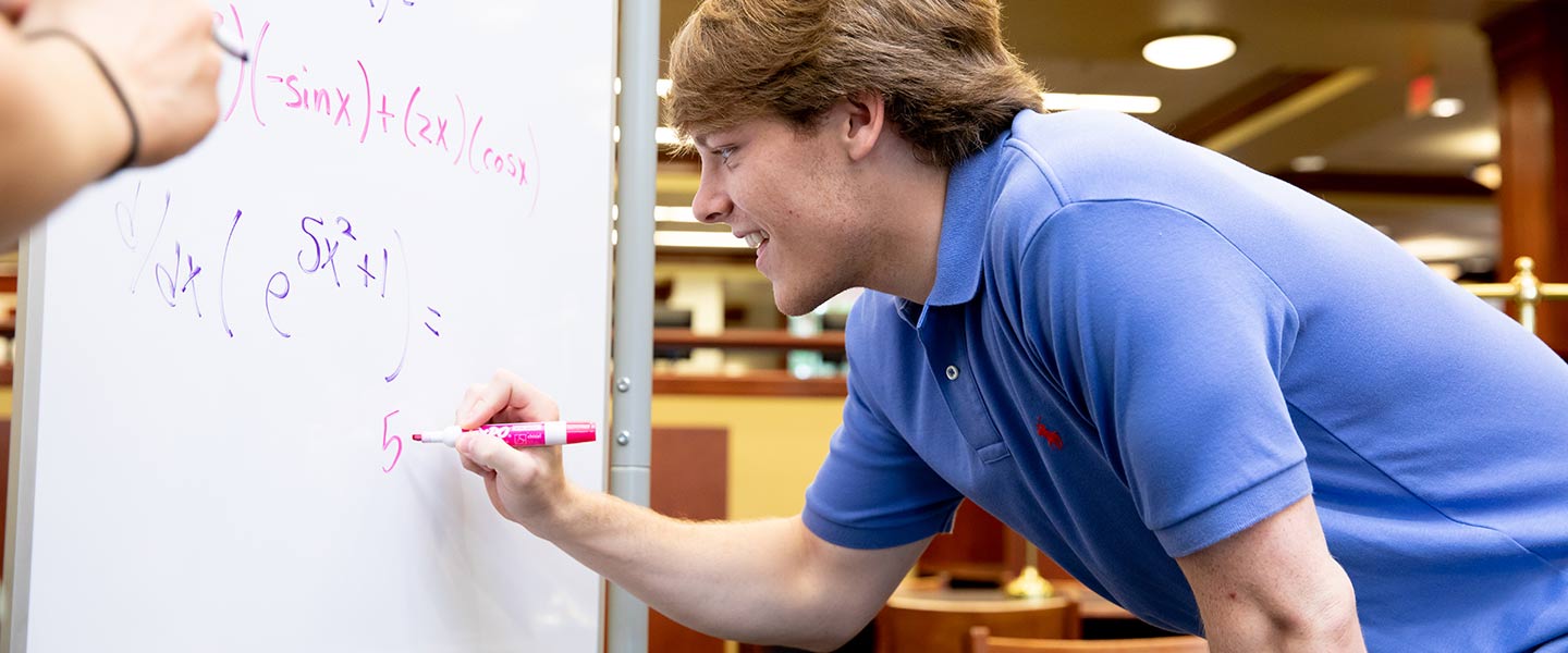 Student writing a math problem on a white board