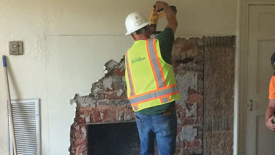 construction worker removing plaster to reveal a fireplace