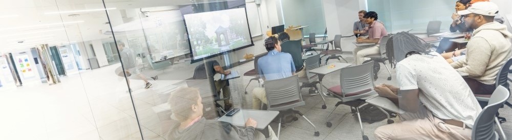 students sitting attentive in a bright, glass-walled classroom