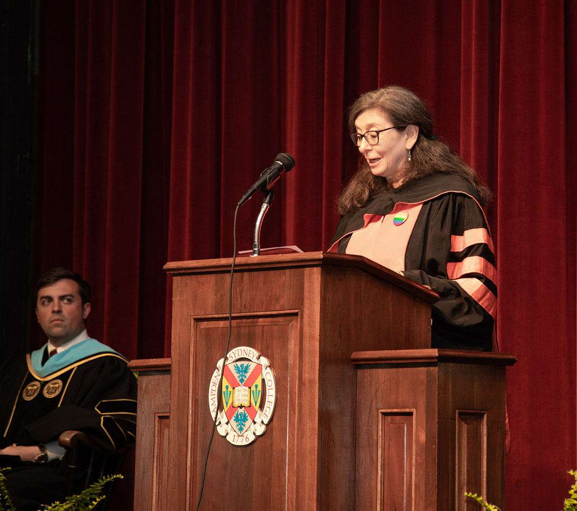 Dr. Sarah Hardy in regalia addresses the faculty and student bodies at the podium