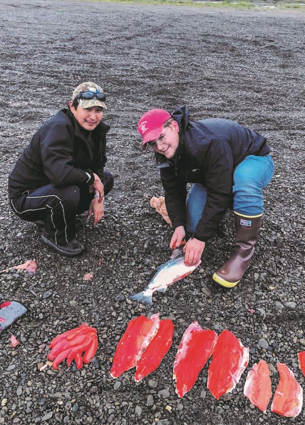 Student and elder fileting salmon on a rocky beach