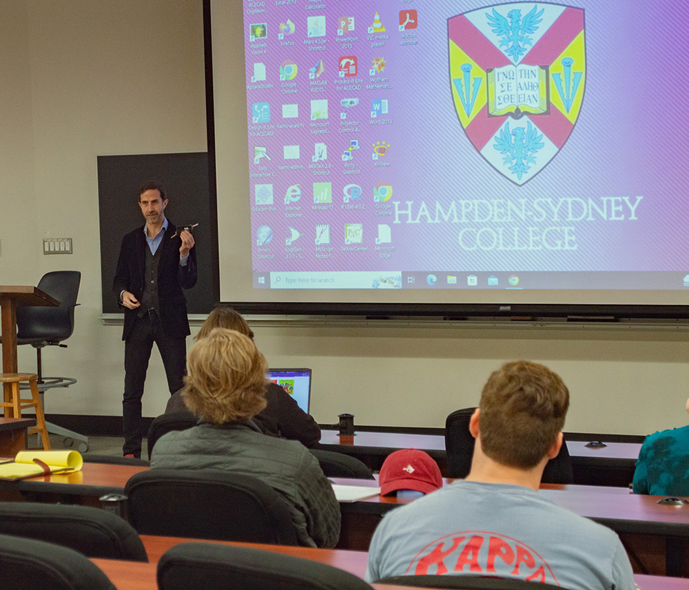 Dr. King giving a lecture in a classroom with H-SC logo in background
