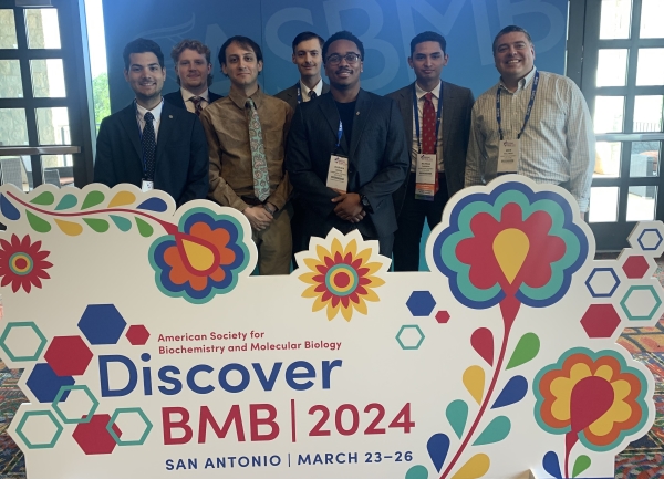 students and professor standing beside a "BMB" conference sign