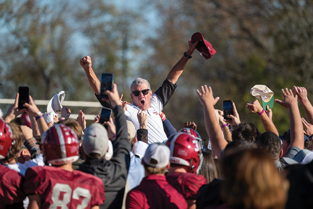 Coach Favrtecheering atop students' shoulders after a football game