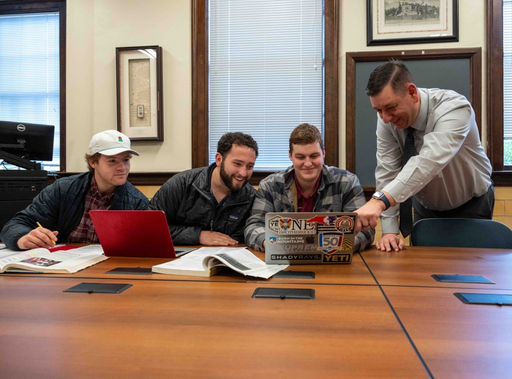 Professor Matyus and 3 students collaborate at a table together on their computers