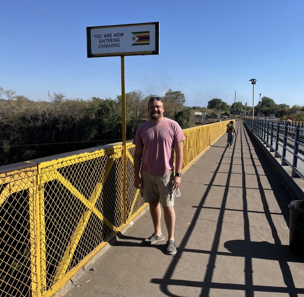 Carter Spawn on a bridge in front of a sign that says, "Zimbabwe"